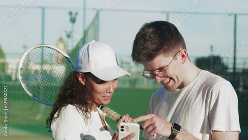 4K. A guy and a girl tennis players communicate by looking at the phone on the tennis court.