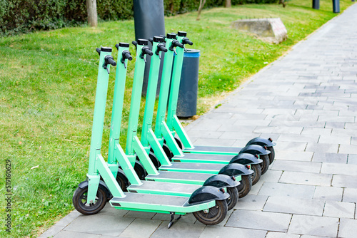 Station of green rental electric scooters for easier travelling or commute on a paved sidewalk in an urban area