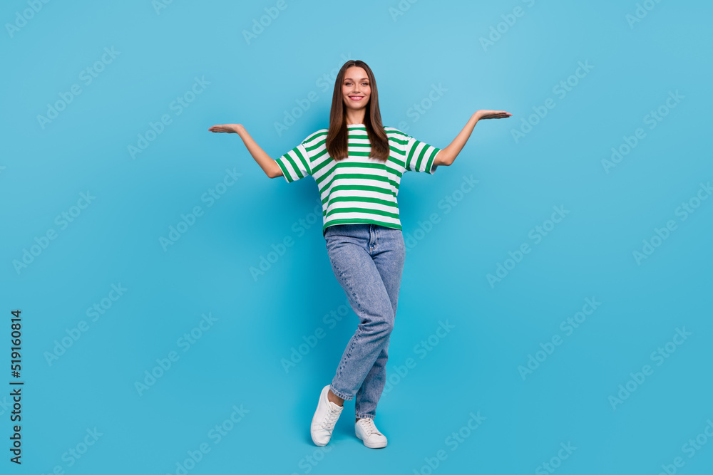 Full size photo of optimistic young lady hold empty space wear t-shirt jeans shoes isolated on blue color background