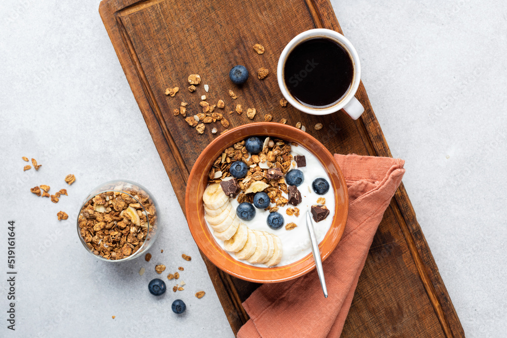 Breakfast bowl with yogurt, granola and fruits served with cup of black coffee on a wooden serving board, top view, copy space Breakfast bowl with yogurt, granola and fruits served with cup of black coffee on a wooden serving board, top view, copy space