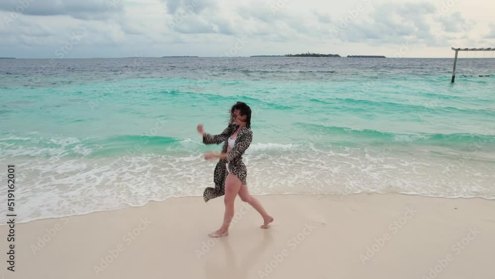 Aerial shot of cheerful woman dancing on a beach, skyline and turquoise waves of Indian ocean in Maldives. Concept of trip to dream Aerial shot of cheerful woman dancing on a beach, skyline and turquoise waves of Indian ocean in Maldives. Concept of trip to dream