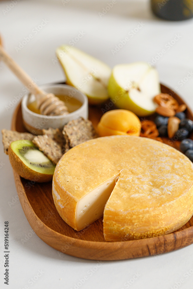 French Reblochon cheese on wooden plate with fruits and honey. Cheese plate, dish. Cutting cheese. French Reblochon cheese on wooden plate with fruits and honey. Cheese plate, dish. Cutting cheese.