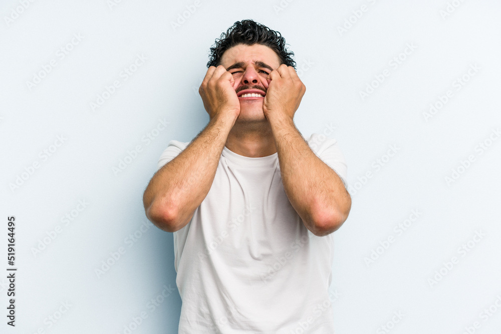 Young caucasian man isolated on blue background crying, unhappy with something, agony and confusion concept. Young caucasian man isolated on blue background crying, unhappy with something, agony and confusion concept.