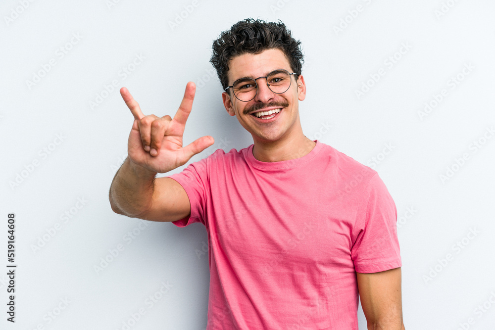 Young caucasian man isolated on blue background showing a horns gesture as a revolution concept. Young caucasian man isolated on blue background showing a horns gesture as a revolution concept.
