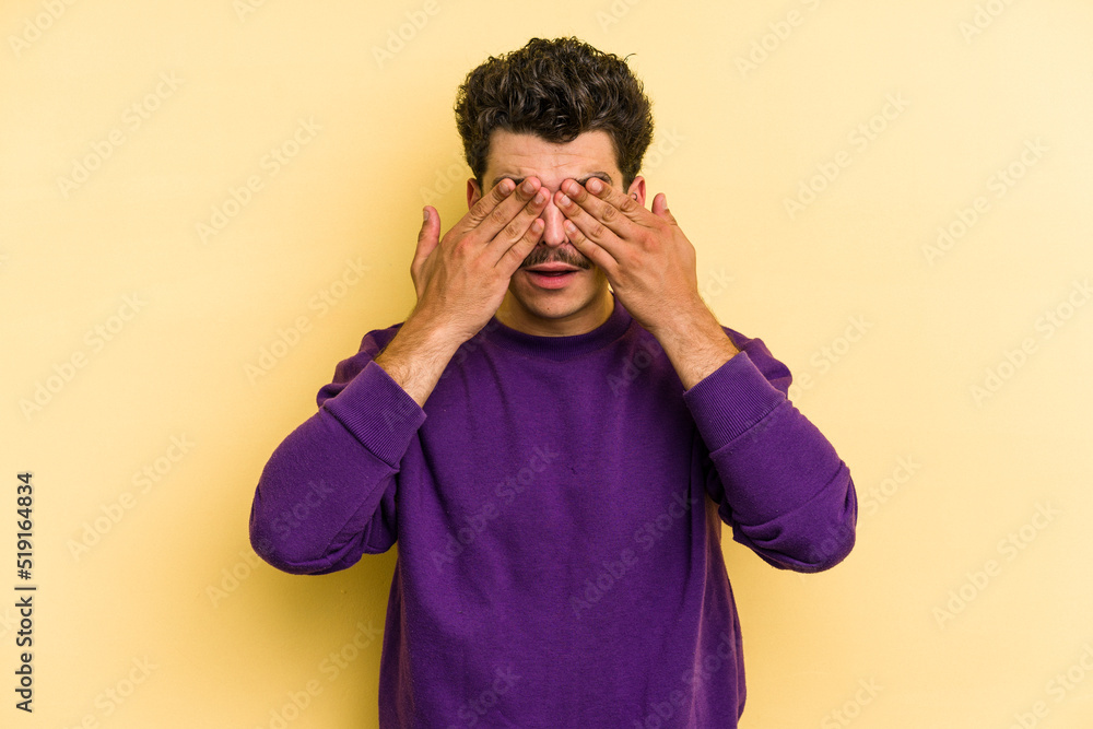 Young caucasian man isolated on yellow background afraid covering eyes with hands. Young caucasian man isolated on yellow background afraid covering eyes with hands.