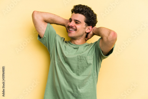 Young caucasian man isolated on yellow background feeling confident, with hands behind the head. © Asier