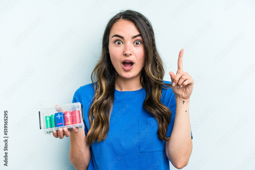 Young caucasian woman holding batteries isolated on blue background having some great idea, concept of creativity. Young caucasian woman holding batteries isolated on blue background having some great idea, concept of creativity.