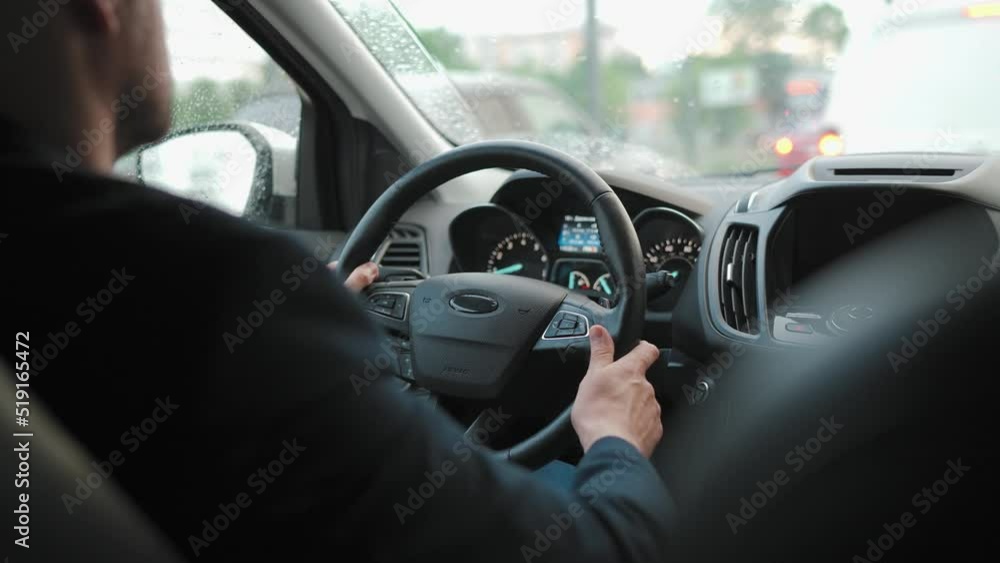 Man drives a car along the road in the city during the rain. View from behind the driver's shoulder Man drives a car along the road in the city during the rain. View from behind the driver's shoulder