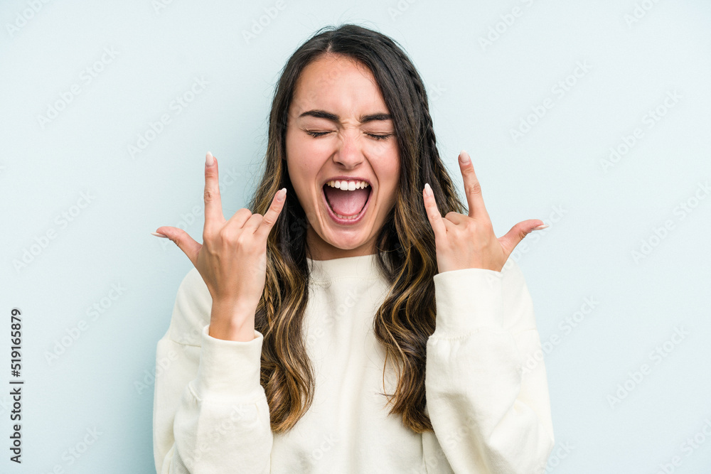 Young caucasian woman isolated on blue background showing a horns gesture as a revolution concept. Young caucasian woman isolated on blue background showing a horns gesture as a revolution concept.