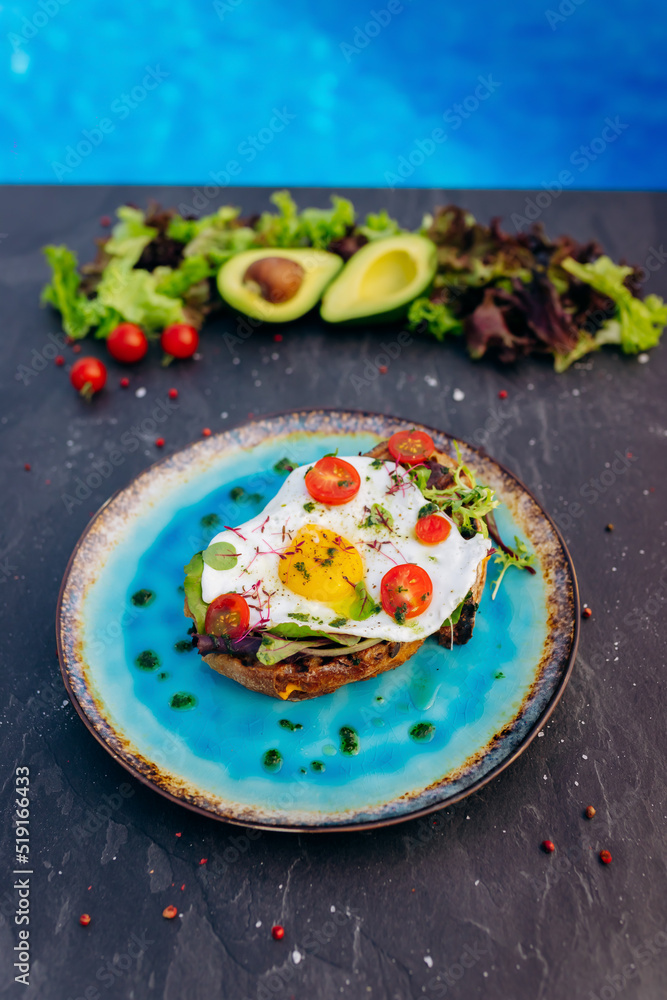 French Toast with Fried Egg , bacon, salad and tomatoes served on blue plate. Tasty Breakfast concept French Toast with Fried Egg , bacon, salad and tomatoes served on blue plate. Tasty Breakfast concept