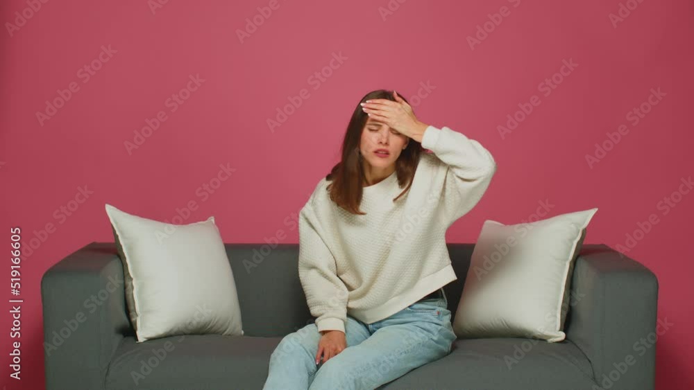 Sick tired young girl touching forehead having headache migraine, sitting on sofa. Ill woman's head hurts Sick tired young girl touching forehead having headache migraine, sitting on sofa. Ill woman's head hurts