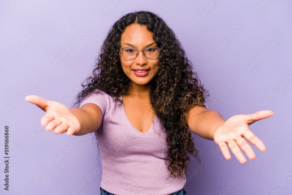 Young hispanic woman isolated on purple background showing a welcome expression. Young hispanic woman isolated on purple background showing a welcome expression.