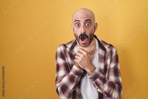 Hispanic man with beard standing over yellow background shouting and suffocate because painful strangle. health problem. asphyxiate and suicide concept.
