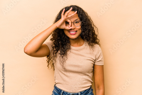 Young hispanic woman isolated on beige background excited keeping ok gesture on eye.