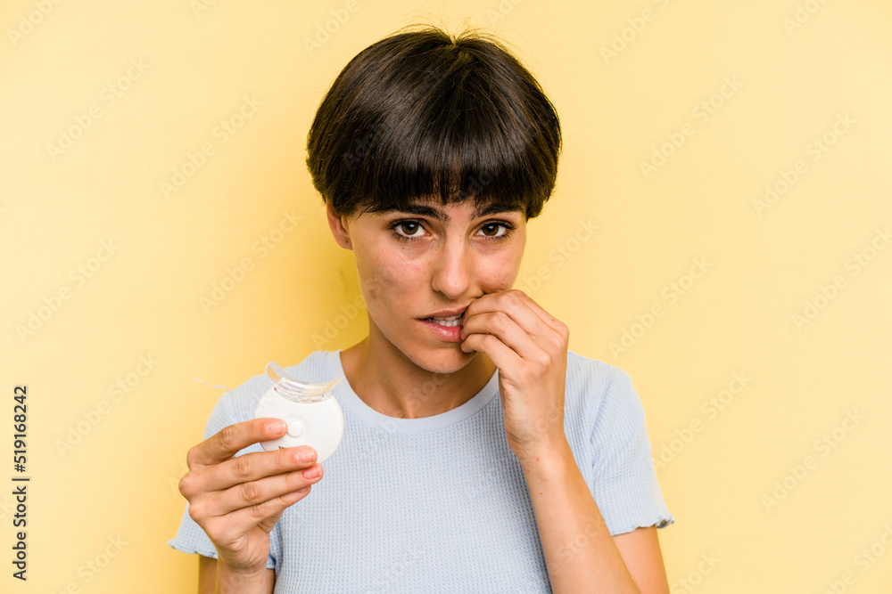 Young caucasian woman holding teeth whitener isolated on yellow background biting fingernails, nervous and very anxious. Young caucasian woman holding teeth whitener isolated on yellow background biting fingernails, nervous and very anxious.