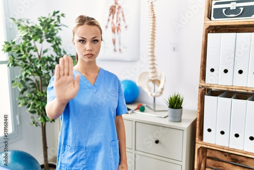 Young caucasian woman working at pain recovery clinic doing stop sing with palm of the hand. warning expression with negative and serious gesture on the face.