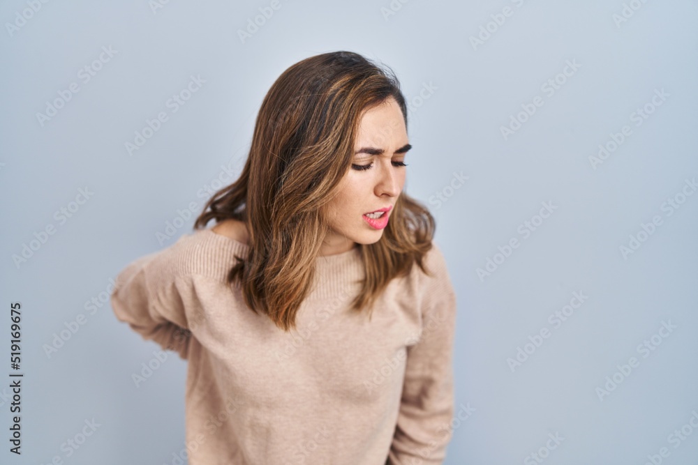 Young woman standing over isolated background suffering of backache, touching back with hand, muscular pain Young woman standing over isolated background suffering of backache, touching back with hand, muscular pain