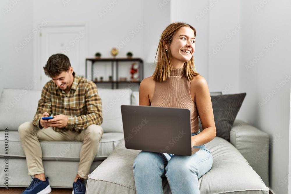 Young hispanic couple smiling happy using laptop and smartphone sitting on the sofa at home. Young hispanic couple smiling happy using laptop and smartphone sitting on the sofa at home.