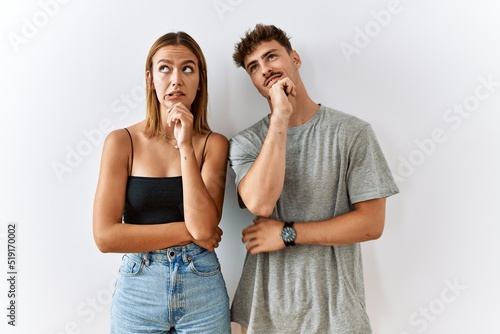 Young beautiful couple standing together over isolated background thinking worried about a question, concerned and nervous with hand on chin