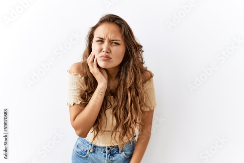 Beautiful hispanic woman standing over isolated while background touching mouth with hand with painful expression because of toothache or dental illness on teeth. dentist © Krakenimages.com