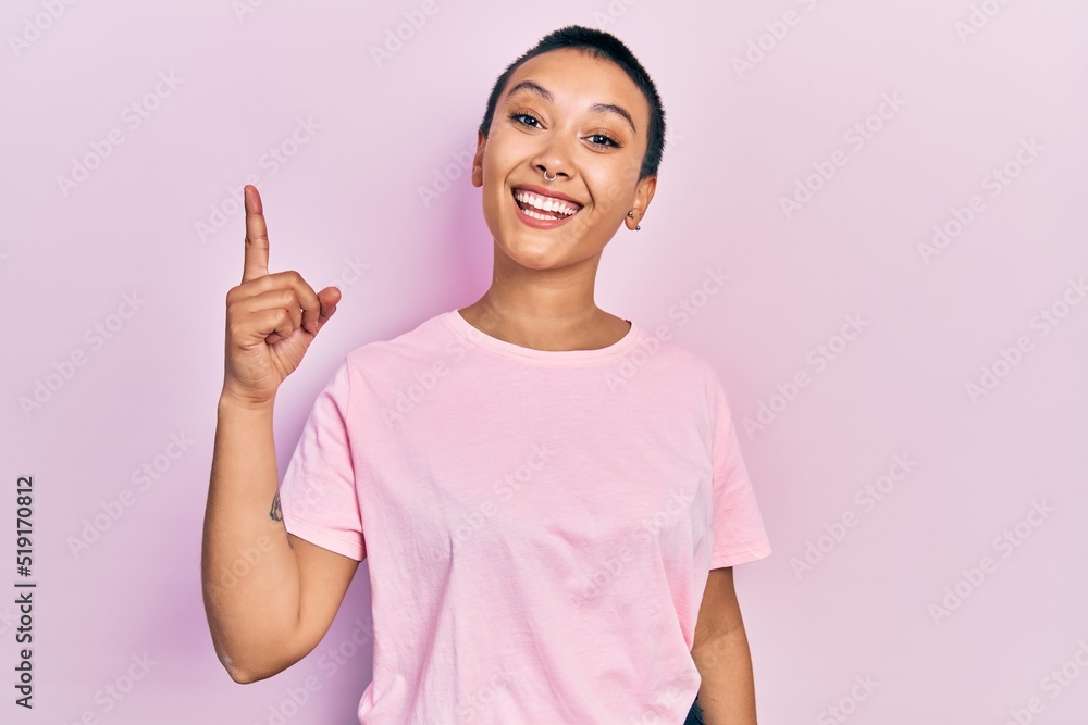 Beautiful hispanic woman with short hair wearing casual pink t shirt showing and pointing up with finger number one while smiling confident and happy. Beautiful hispanic woman with short hair wearing casual pink t shirt showing and pointing up with finger number one while smiling confident and happy.