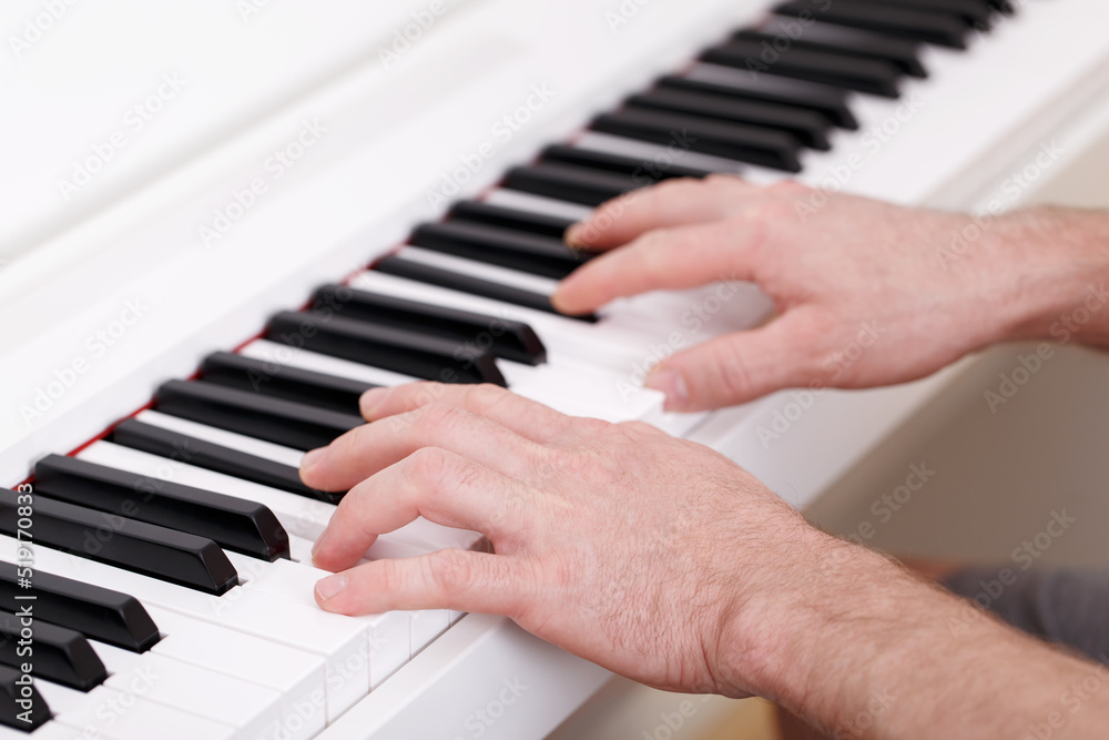 Fototapeta premium Young man playing on white modern piano, home learning, music education, composing