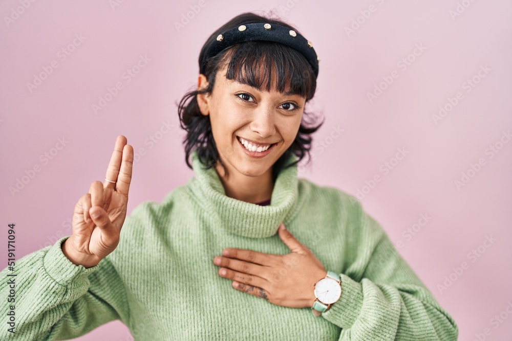 Young beautiful woman standing over pink background smiling swearing with hand on chest and fingers up, making a loyalty promise oath Young beautiful woman standing over pink background smiling swearing with hand on chest and fingers up, making a loyalty promise oath