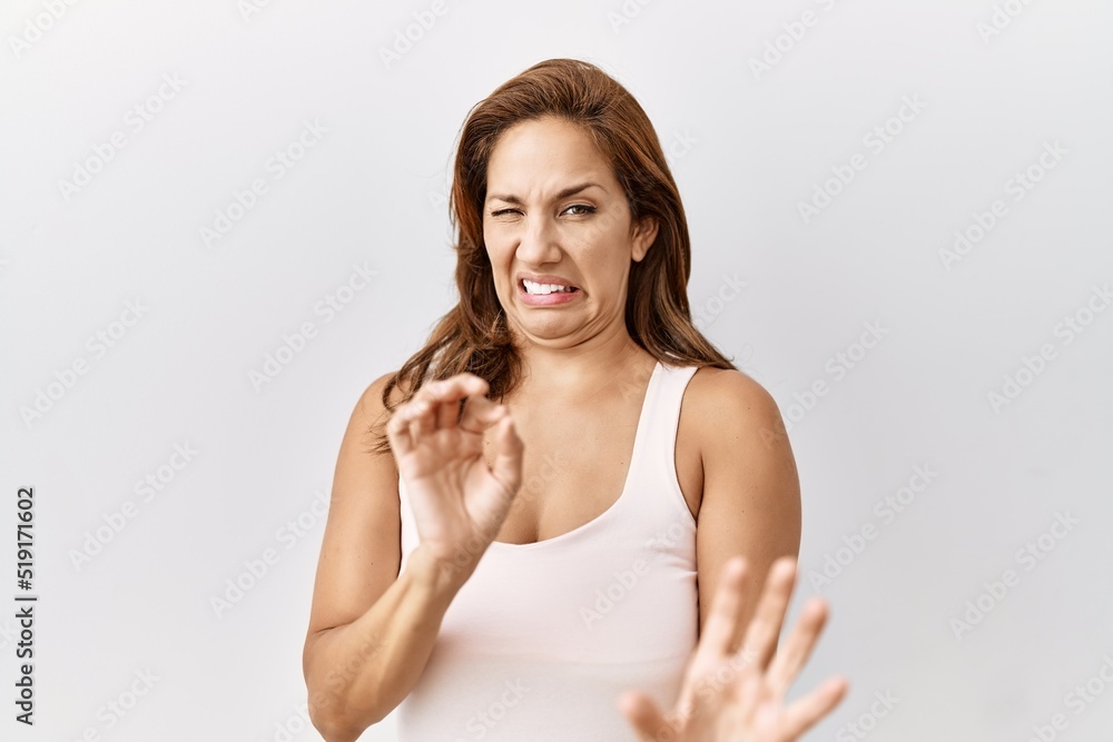 Middle age hispanic woman standing over isolated background disgusted expression, displeased and fearful doing disgust face because aversion reaction. with hands raised Middle age hispanic woman standing over isolated background disgusted expression, displeased and fearful doing disgust face because aversion reaction. with hands raised