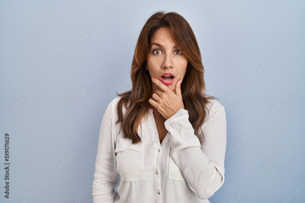 Hispanic woman standing over isolated background looking fascinated with disbelief, surprise and amazed expression with hands on chin Hispanic woman standing over isolated background looking fascinated with disbelief, surprise and amazed expression with hands on chin
