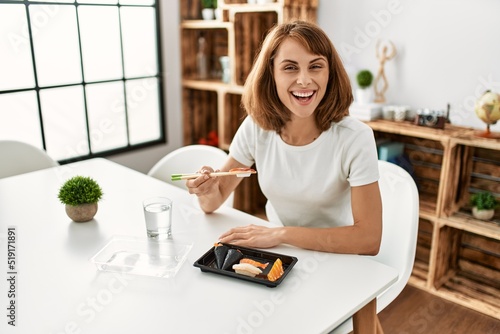 Young caucasian woman eating sushi sitting on table at home