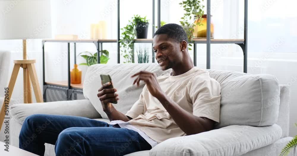 African american man video chatting using mobile phone while sitting on sofa at home African american man video chatting using mobile phone while sitting on sofa at home