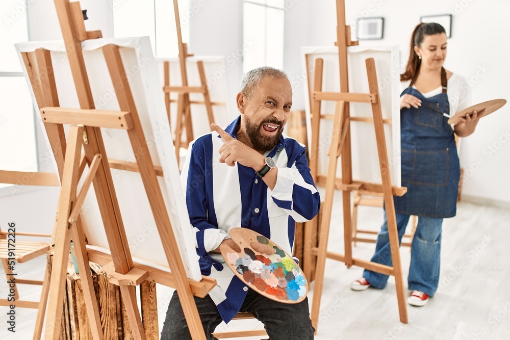 Senior artist man at art studio pointing aside worried and nervous with forefinger, concerned and surprised expression Senior artist man at art studio pointing aside worried and nervous with forefinger, concerned and surprised expression