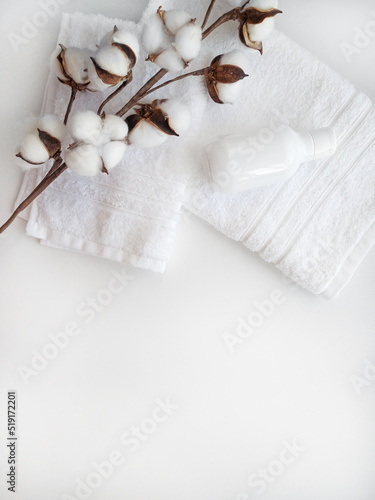 White towels with cotton flower branch and white plastic bottle for cosmetics on the white background.