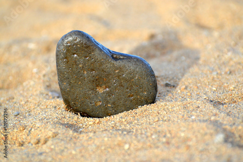 Heart shape stone against background of beach. Summer sunny day. Love, wedding and Valentine day concept. Finding beautiful and interesting stones. Beach vacation. 