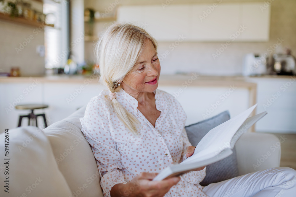 Obraz premium Senior woman sitting on sofa and reading book at home