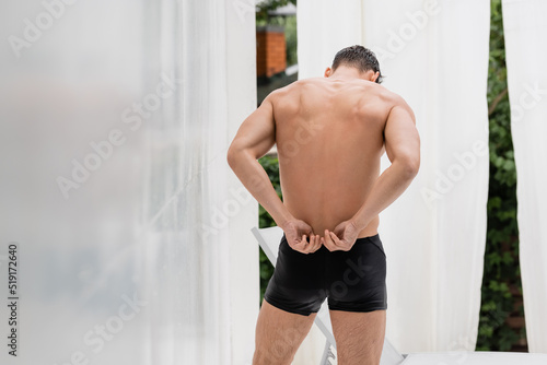 back view of sportive man adjusting wet swimming trunks.