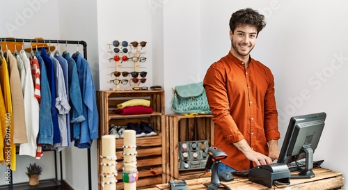 Young hispanic shopkeeper man smiling happy working at clothing store. photo