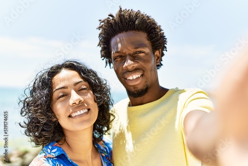 Young beautiful couple smiling happy and hugging making selfie by the camera at the beach.