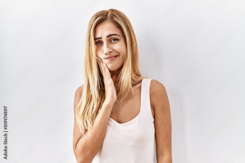 Blonde beautiful young woman standing over white isolated background touching mouth with hand with painful expression because of toothache or dental illness on teeth. dentist Blonde beautiful young woman standing over white isolated background touching mouth with hand with painful expression because of toothache or dental illness on teeth. dentist