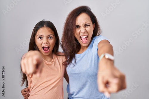 Young mother and daughter standing over white background pointing displeased and frustrated to the camera  angry and furious with you