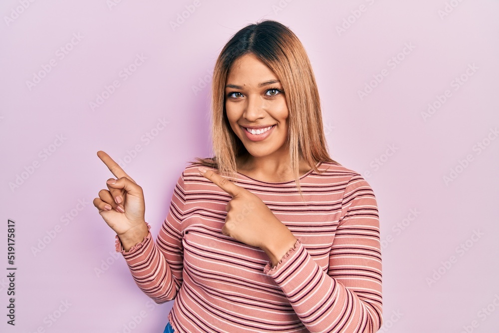 Beautiful hispanic woman wearing casual striped sweater smiling and looking at the camera pointing with two hands and fingers to the side. Beautiful hispanic woman wearing casual striped sweater smiling and looking at the camera pointing with two hands and fingers to the side.