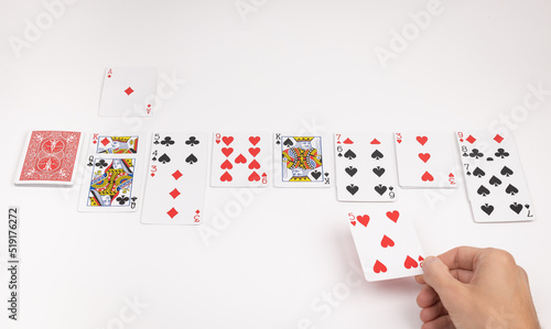 Person playing solitaire on white background with standard playing cards