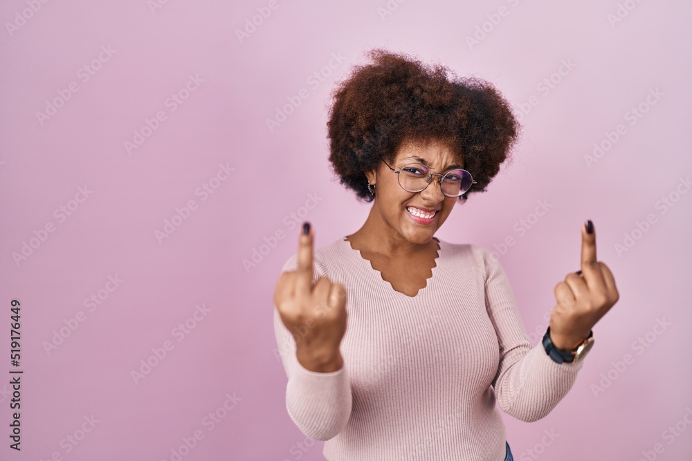 Young african american woman standing over pink background showing middle finger doing fuck you bad expression, provocation and rude attitude. screaming excited Young african american woman standing over pink background showing middle finger doing fuck you bad expression, provocation and rude attitude. screaming excited