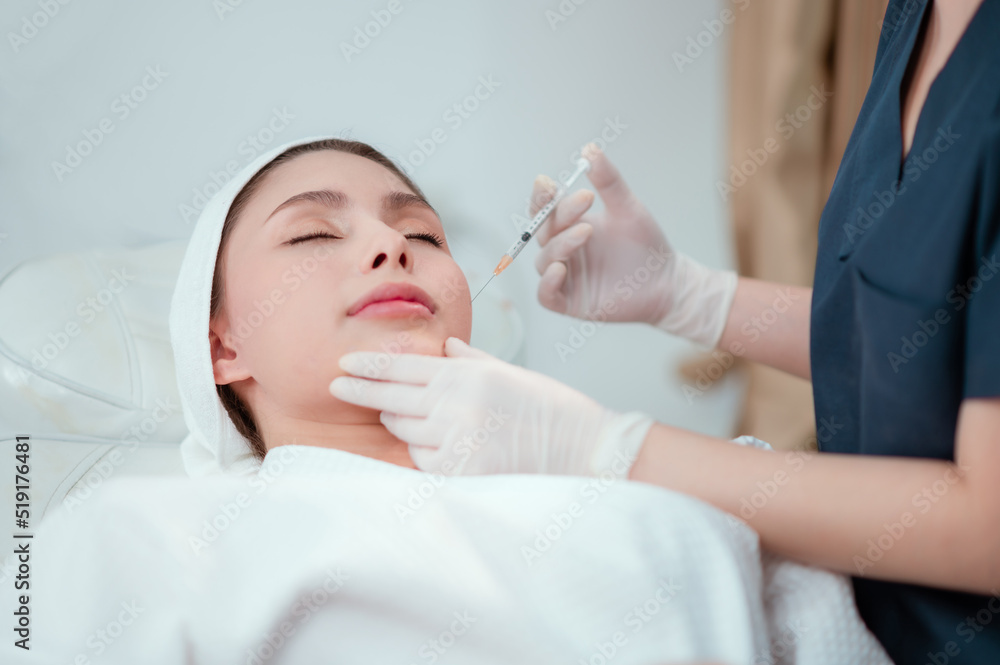 Fototapeta premium Girl beautician makes injections on the lips and face of a beautiful woman in a cosmetic wedge.