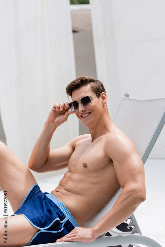 happy man with athletic body adjusting sunglasses in deck chair outdoors. happy man with athletic body adjusting sunglasses in deck chair outdoors.