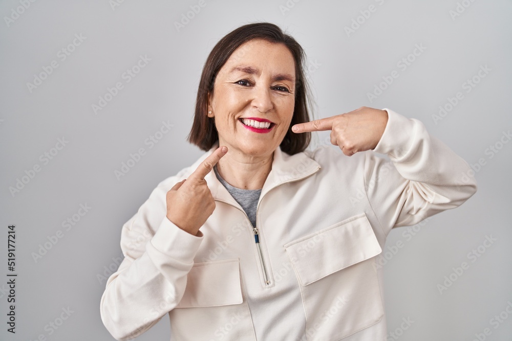 Middle age hispanic woman standing over isolated background smiling cheerful showing and pointing with fingers teeth and mouth. dental health concept. Middle age hispanic woman standing over isolated background smiling cheerful showing and pointing with fingers teeth and mouth. dental health concept.