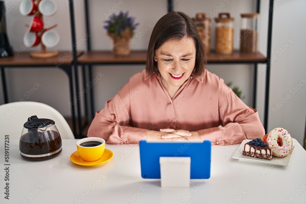 Middle age woman having breakfast using touchpad sitting on table at home Middle age woman having breakfast using touchpad sitting on table at home