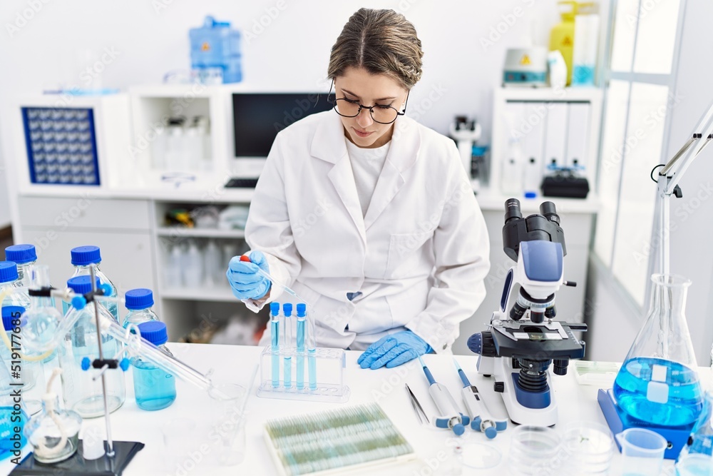 Young hispanic woman wearing scientist uniform using pipette at laboratory Young hispanic woman wearing scientist uniform using pipette at laboratory