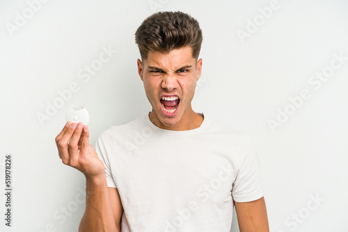 Young caucasian man hand sling isolated on white background screaming very angry and aggressive.