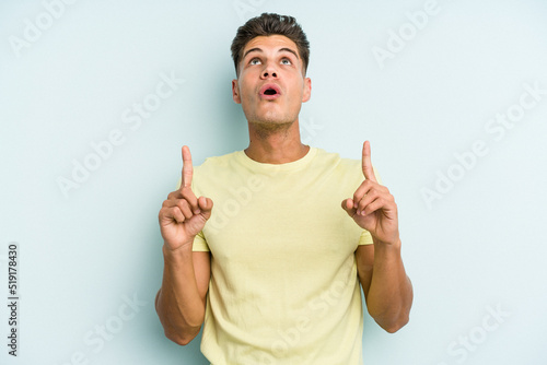 Young caucasian man isolated on blue background pointing upside with opened mouth.